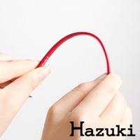 一雙手拿著一條彎曲的亮紅色鏡框，鏡框上印有「Hazuki」字樣。