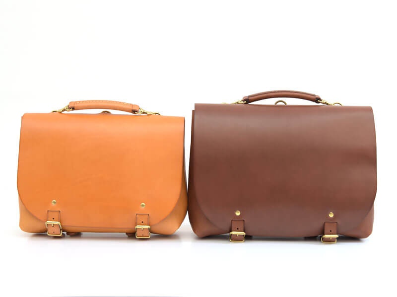 兩款職人手作皮革雙扣兩用側背包，一款為淺棕色，另一款為深棕色，皆為真皮材質，配有金色金屬扣環及提把。