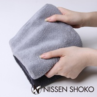 兩隻手正在展示一條淺灰色的長毛巾，其材質柔軟，毛圈細緻。下方疊著一條深灰色的同款毛巾。