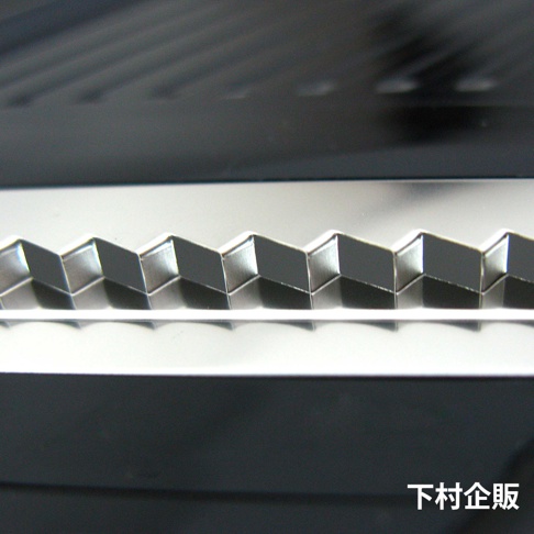 銀色金屬材質的四合一刨絲器，展示其鋸齒狀的刀刃特寫，刀刃呈 Zig-zag 形狀，表面光滑反光，呈現出精緻的工藝細節。