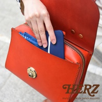 日本HERZ手工皮革包，一個裝有手機和藍色方巾的紅色翻蓋包，包上有金色旋轉鎖扣和品牌標誌。