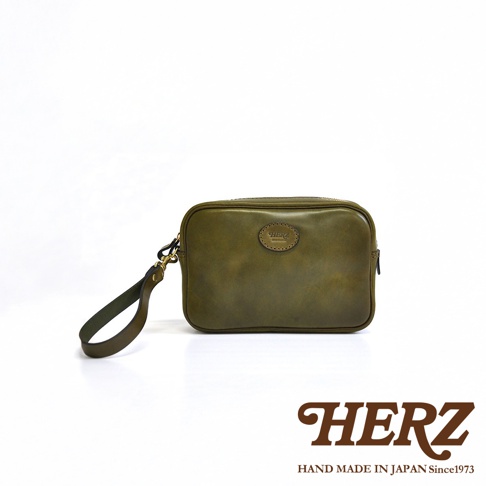 橄欖綠皮革手提包，配有可拆卸扣環和圓形品牌標誌。