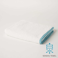 白色長纖毛巾，邊緣滾有藍色滾邊，質地蓬鬆柔軟，帶有緞澤光澤。