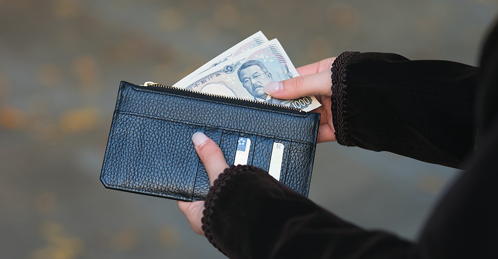 一個人正在從黑色荔枝紋皮革長夾中取出日圓鈔票，長夾上有卡槽。