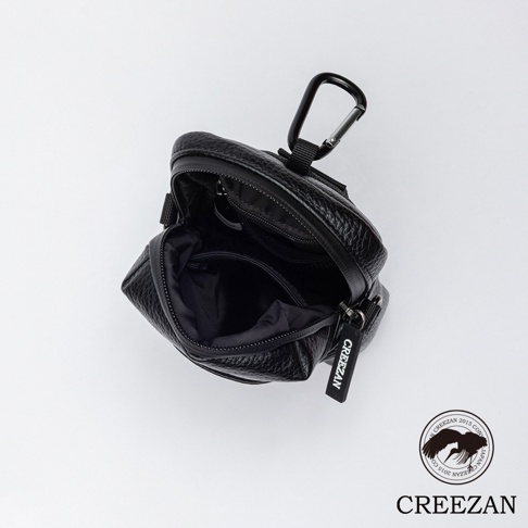 一個黑色的皮革紋理高爾夫球收納腰包，有拉鍊開合，頂部有一個登山扣，側面有一個印有品牌名稱的吊牌。