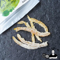 一堆金黃色、帶有白色糖粉的柑橘果皮乾，呈彎曲的條狀，擺放在深灰色紋理的背景上。
