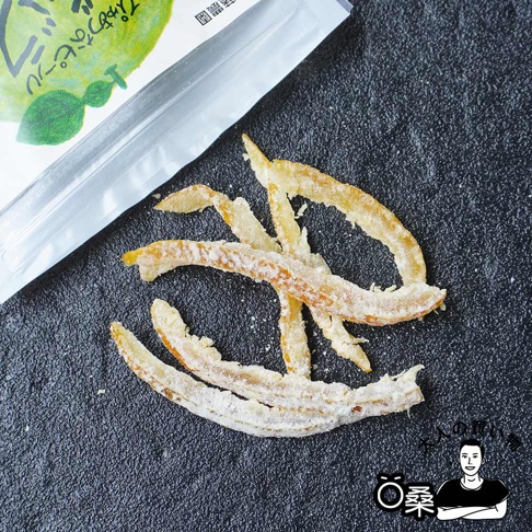 一堆金黃色、帶有白色糖粉的柑橘果皮乾，呈彎曲的條狀，擺放在深灰色紋理的背景上。
