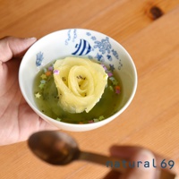 白瓷小碗盛著翠綠色果凍，中間漂浮著一朵黃綠色奇異果切片製成的玫瑰花，周圍散落著糖粉星星。碗內側裝飾著藍色海魚和氣泡圖案。