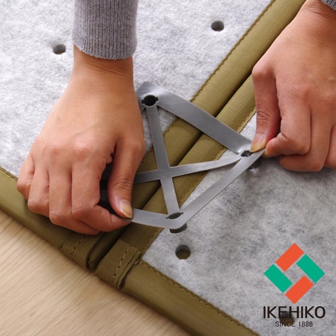 兩隻手正在將灰色塑料製成的藺草榻榻米專用連結器扣合在淺灰色氈狀材質和卡其色織物邊緣的榻榻米上。