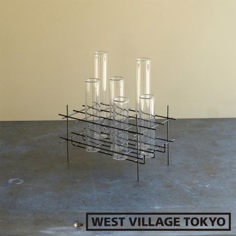 黑色金屬支架，帶有六個透明玻璃試管狀花器，置於深色桌面，背景為淡黃色牆面。