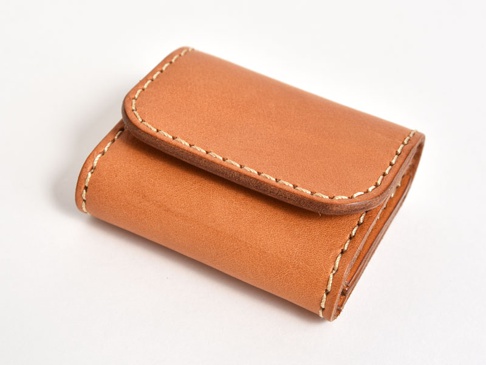棕色皮革雙折收納零錢包，表面光滑，以米白色縫線手工縫製，呈現簡約設計。
