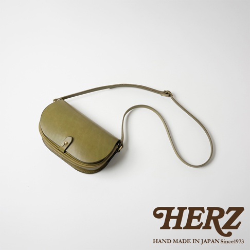 橄欖綠皮革迷你馬鞍包，採用職人手作工藝，設有翻蓋式開口與金屬扣，搭配可調式皮革長背帶。