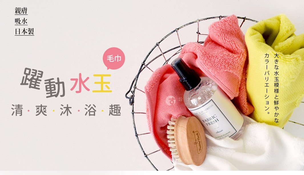 金屬網籃內有三條無撚紗毛巾，分別為粉紅色、黃色和白色。籃子中還有一瓶噴霧式織物清新劑和一個木製毛刷。