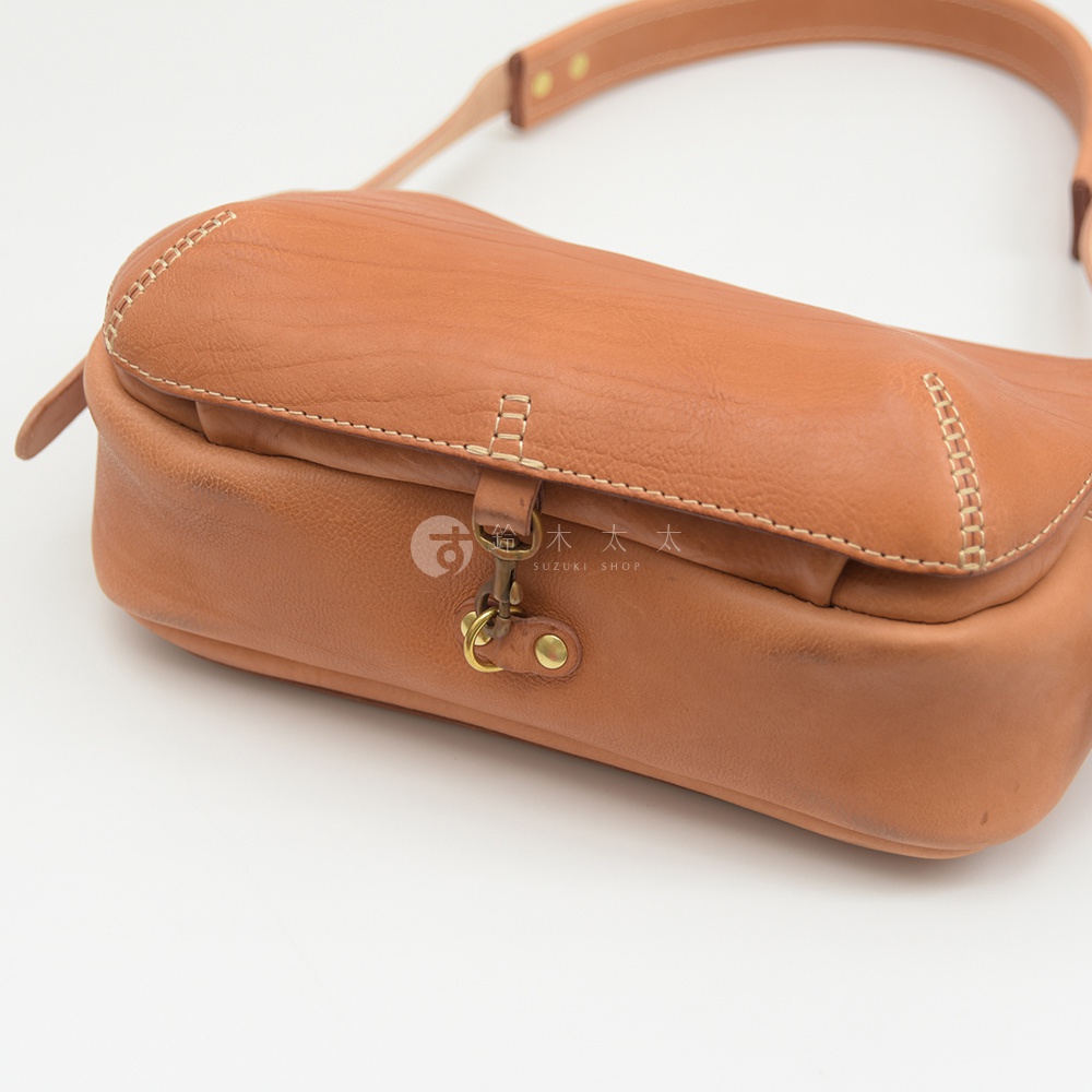 棕色皮革製作的郵差包，具有大容量設計，包蓋處有金屬扣環和鉚釘裝飾，包身及肩帶縫線明顯。