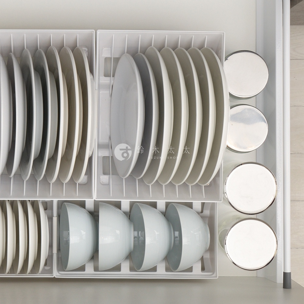 抽屜式餐碗收納架內整齊擺放著多個白色盤子和碗，盤子被分隔開，碗則呈一排擺放，收納架呈現白色。