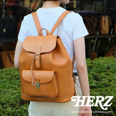 棕褐色皮革製作的經典後背包，配有翻蓋、束繩、前袋和金屬扣環，由日本職人手工縫製。
