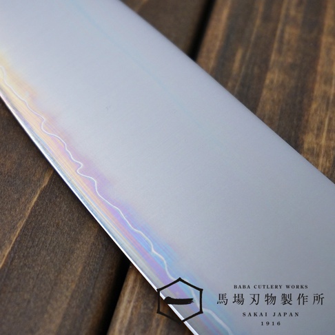 [景清] Chromax鋼三德刀，展示其光滑的銀色金屬刀刃，帶有彩虹般的光澤紋理。刀刃靠近木紋背景。