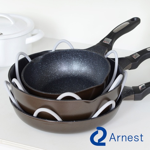 三個疊放的鍋具，中間夾有白色防刮保護墊，最上層鍋具為黑色帶斑點，底部鍋具為棕色。