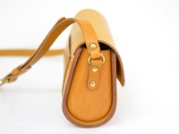 職人手作的淺棕色皮革馬鞍包，具有寬版可調式肩帶和金屬寬扣帶，搭配圓潤的包身設計，展現經典復古風格。