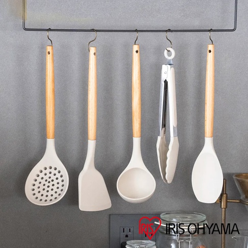 五件白色矽膠廚房用具，包含漏勺、鍋鏟、湯勺、夾子和飯勺，皆配有木質手柄，懸掛於黑色收納架上。