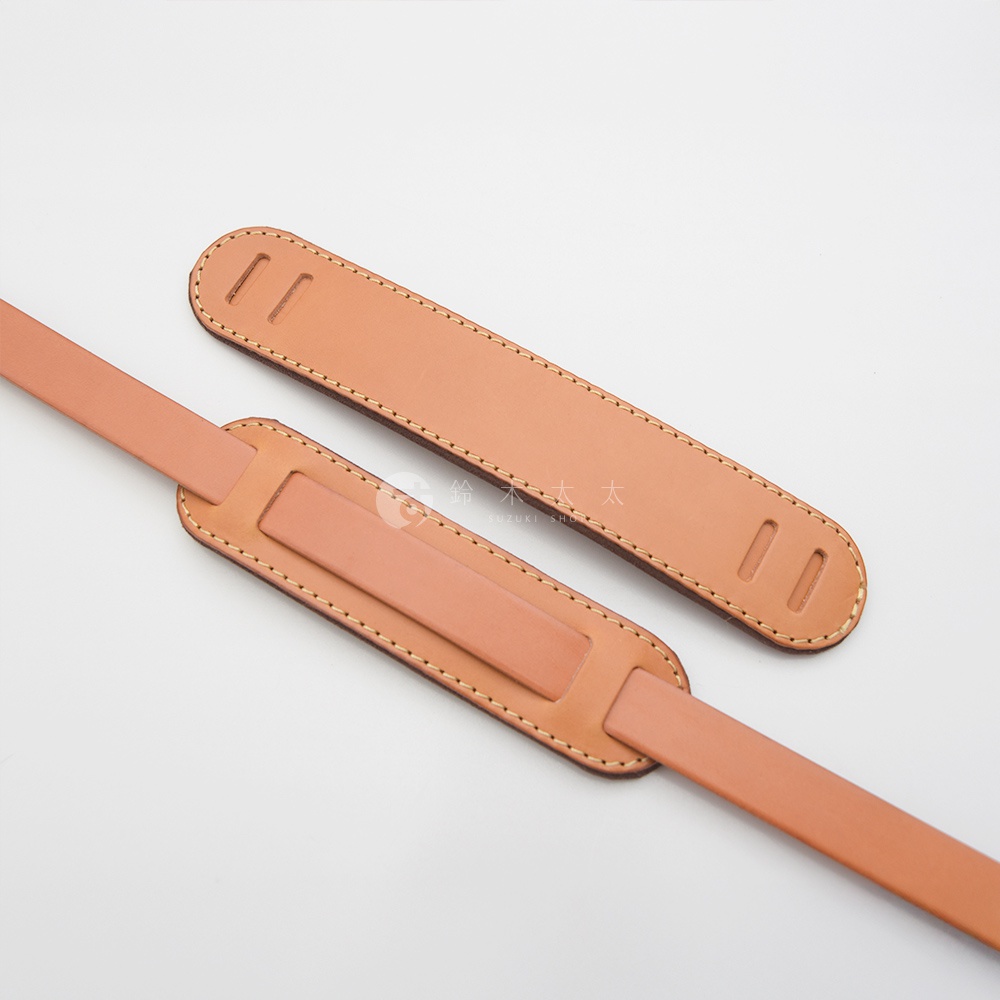 兩條淺棕色皮革肩墊，帶有縫線裝飾，其中一條肩墊上有兩個長方形孔。