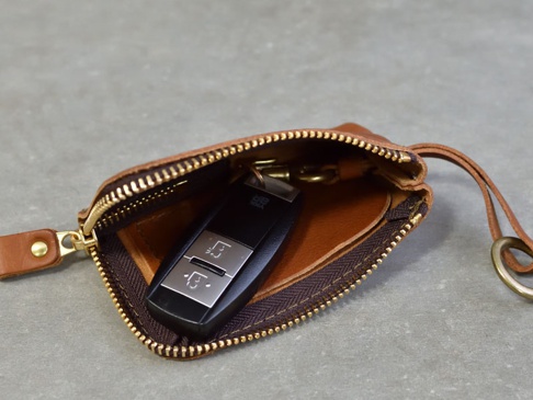 職人手作皮革鑰匙包，棕色，拉鍊開合，內含黑色汽車遙控器，附有皮革繫繩和掛環。