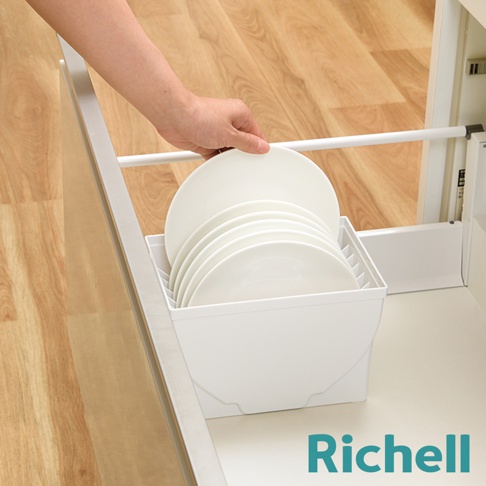 手正在將一疊白色盤子放入一個白色抽屜式餐盤收納架中，收納架置於廚房抽屜內，背景為木紋地板。