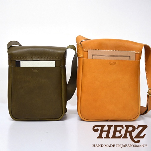 兩款日本 HERZ 職人手作皮革軟皮直式斜背包，一款為橄欖綠色，另一款為橘黃色，皆有前置收納袋，並印有 HERZ LOGO。