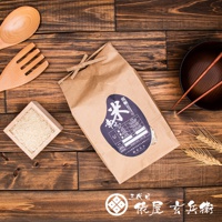 淺棕色紙袋裝著北海道夢美人米，上面貼有深藍色標籤，標籤上印有日文文字及產品資訊。一旁有木質小方盒裝著少量米粒，以及木製湯勺和叉子。背景為木紋桌面，右側有深色碗和兩根紅色筷子，以及兩支麥穗。