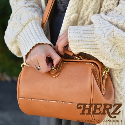 皮革製成的棕色口金醫生單肩包，帶有白色縫線和金色五金件。