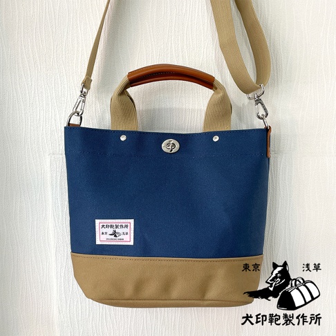 犬印純棉帆布兩用雙色托特包，主體為海軍藍，底部為卡其色，配有皮革提把與帆布肩帶，設有銀色旋轉鎖扣。