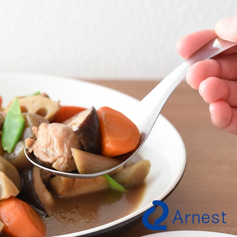一只手拿著不鏽鋼湯匙，湯匙盛著燉煮的雞肉、香菇、紅蘿蔔、蓮藕和豌豆，湯匙帶有細孔設計，湯汁從孔中流下。