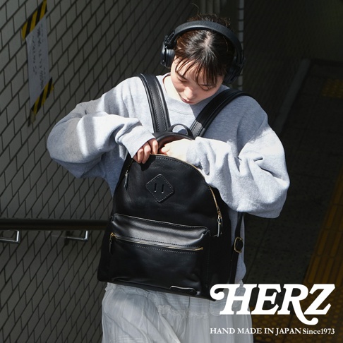 職人手作黑色皮革後背包，採用簡約休閒風格設計，正面有拉鍊口袋和菱形皮革飾片，搭配金屬拉鍊，適合日常使用。
