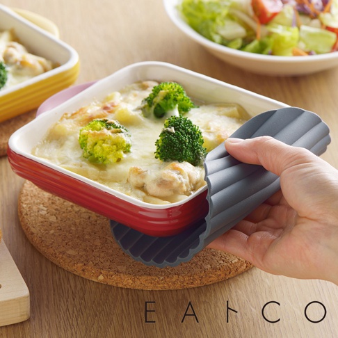 灰色波浪紋隔熱墊，用於夾取裝有焗烤雞肉與花椰菜的紅色烤盤。