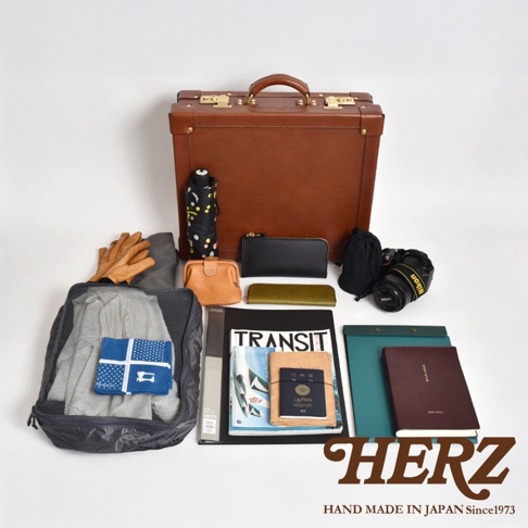 職人手作皮革英倫風便攜手提行李箱，搭配黑色傘、咖啡色皮革手套、卡夾、筆記本、護照、相機及收納袋，呈現精緻旅途用品組合。