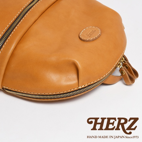 職人手作皮革圓角後背包，採用鞣製皮革材質，呈現溫潤的焦糖棕色。大開口設計，附有雙拉鍊頭，細緻車縫線與圓形皮革標誌，展現精緻工藝。