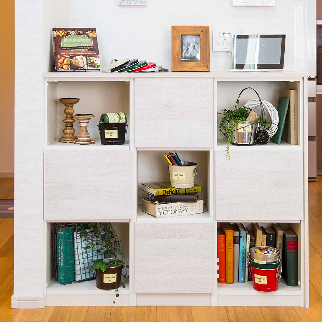 模式B： 一個白色木紋儲物櫃，展示著各種家居裝飾品和書籍，包含一個裝有綠色植物的迷你桶，以及多個不同尺寸的籃子和蠟燭台。