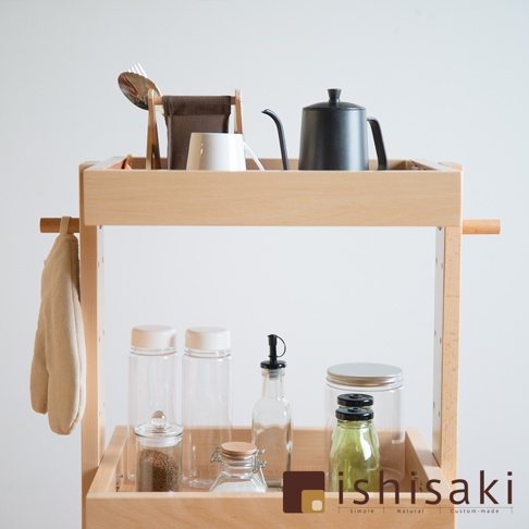 淺木色木製收納推車，頂層擺放著咖啡壺、馬克杯、餐具，側邊掛有淺褐色布巾；下層則有各式玻璃罐、瓶裝調味料。