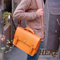 駝色皮革手提/斜背包，正面有兩個皮帶扣和一個鎖扣，搭配同色系皮革提把和可拆卸斜背帶。