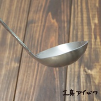 不鏽鋼萬用湯勺，勺柄和勺身均為銀色不鏽鋼材質，勺身呈弧形，背景為木紋桌面。