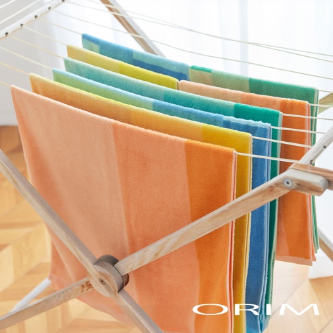 HARUKA 今治耐用絢彩拼接毛巾，展示多條毛巾，呈現橘色、黃色、藍色、綠色等漸層和拼接色彩，材質柔軟，懸掛於木質晾衣架上。