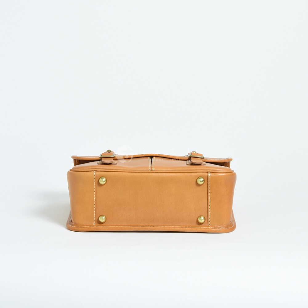 職人手作皮革單肩包，採用淺棕色皮革材質，設有雙扣環與金屬腳釘，風格簡約。