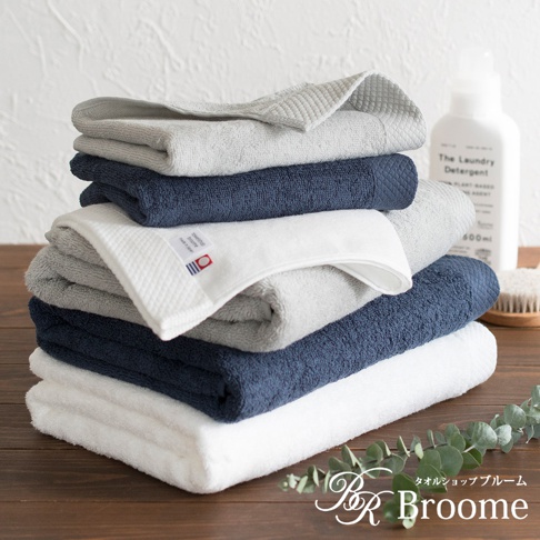 疊放的今治純棉長毛巾，有白色、淺灰色和深藍色。其中一條白色毛巾有菱紋織法和品牌標籤，顯示「towelshop broome made in japan」。
