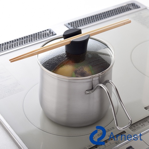 不鏽鋼料理鍋，附玻璃鍋蓋，鍋蓋上放置一雙木筷。鍋身為銀色不鏽鋼材質，有一個金屬提把。鍋內可見食物。