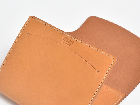 職人手作皮革A6記事本書套，淺棕色牛革，車縫線清晰，內側有兩個卡槽，右側為一體式內頁，左側有品牌標誌。