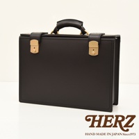 職人手作黑色皮革機師箱，設有金色鎖扣、提把與金屬配件，簡約設計，質感細緻。