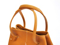 淺棕色皮革托特包，特寫展示包包的提把和邊緣縫線，以及側邊的抽繩設計。