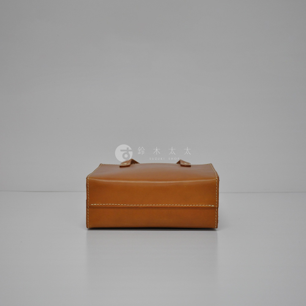 職人手作皮革直式托特包 T-44 XS，以棕褐色皮革製成，方形結構，頂部有提把，側邊及底部有白色縫線裝飾。