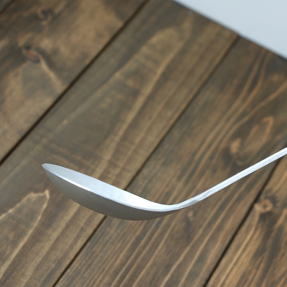 鋁製錘目紋湯勺，銀色，帶有明顯的錘擊紋理，勺柄光滑，置於深色木紋背景上。