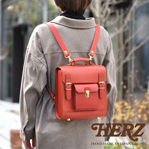 職人手作經典學院風迷你後背包，採用紅色皮革製成，配有金色金屬扣環和旋轉鎖，肩帶亦為紅色皮革。